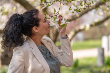 Açık renk ceketli şık bir kadının romantik görüntüsü. Olumlu, bahar havası. Tatlı bir kız nazikçe beyaz bir sakura dalı tutuyor ve çiçeklere bakıp gülümsüyor.