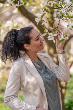Açık renk ceketli şık bir kadının romantik görüntüsü. Olumlu, bahar havası. Tatlı bir kız nazikçe beyaz bir sakura dalı tutuyor ve çiçeklere bakıp gülümsüyor.