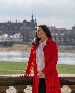 Koyu saçlı, kırmızı paltolu güzel bir bayan turist, Almanya 'nın eski kasabası Dresden' in köprüsünden güzel bir manzaranın tadını çıkarıyor. 