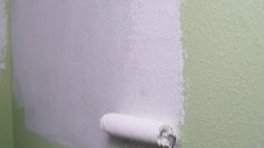 Bir adam yeşil bir duvarı beyaz boyayla silindir kullanarak boyuyor. İnşaatçı, aletler, apartman yenileme.