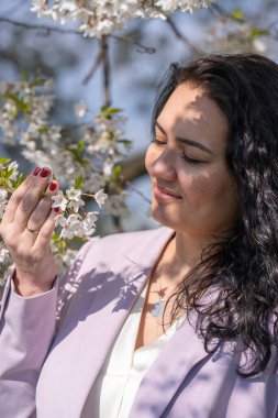 Açık renk ceketli şık bir kadının romantik görüntüsü. Olumlu, bahar havası. Tatlı bir kız nazikçe beyaz bir sakura dalı tutuyor ve çiçeklere bakıp gülümsüyor..