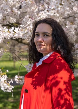 Açık renk ceketli şık bir kadının romantik görüntüsü. Olumlu, bahar havası. Tatlı bir bayan nazikçe beyaz bir sakura dalı tutuyor ve kameraya bakıp gülümsüyor.