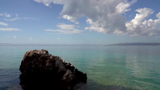 透明平静的大海前景是大海中的一块大石头 克罗地亚的山区景观呈现在地平线上 美丽的云彩 慢动作 — 图库视频影像