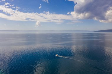 Bir İHA 'dan havadan fotoğraf. Sonsuz mavi, şeffaf denizin ortasında yalnız küçük bir yat. Gökyüzünde büyük bulutlar var. Denizde tatiller.