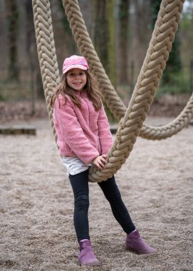 Çocuk salıncağında eğlenen tatlı bir kız. Kalın halatlardan yapılmış bir atlıkarıncada oturuyor. Mutlu çocukluk. 
