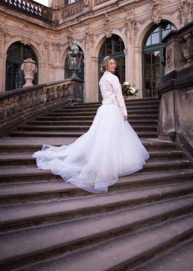 Gelin, taş basamakların üzerinde uzun bir trenle şık bir elbiseyle dikiliyor. Düğün günü.