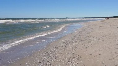 Baltık Denizi 'nde güzel bir deniz manzarası. Dalgalar kumlu sahile hücum ediyor. İnsanlar deniz boyunca sakin bir şekilde yürür. Baltık 'ta Tatil, Huzur, Rahatlama