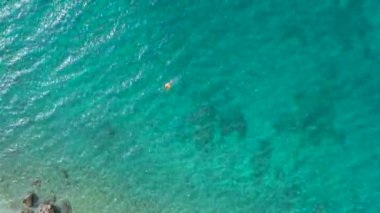 Turkuaz denizin insansız hava aracı görüntüsü. Bir adam denizde yüzüyor. Çam ormanlarının arasında güzel, parlak bir sahil. Makarska. Hırvatistan