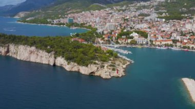 Hırvatistan 'ın Makarska kenti. Şehrin havadan görünüşü. Güzel plajları olan deniz manzarası. Evleri olan bir turist kasabasının insansız hava aracı görüntüsü. Seyahat videosu