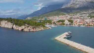 Hırvatistan 'ın Makarska kentinin insansız hava aracı görüntüsü. Tekneler, yatlar, büyük gemiler, şehirdeki evler ve Biokovo 'nun dağlık manzarasıyla güzel bir liman manzarası. Yaz, güneşli gün