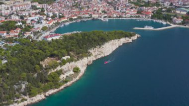 Hırvatistan 'ın Adriyatik Denizi kıyısındaki Makarska kentinde kayalıklardan geçen bir teknenin hava manzarası. Rocky Akdeniz kıyıları berrak turkuaz suyla. 