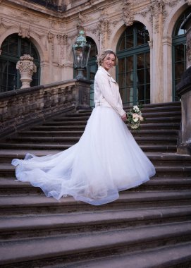 Gelin, düğün gününde uzun trenli güzel bir elbiseyle merdivenlerde duruyor..