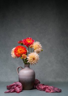 Parlak çiçeklerle dolu bir hayat. Vazoda renkli yıldız çiçekleri, koyu renk şal, gri arka plan. Boşluğu kopyala. 