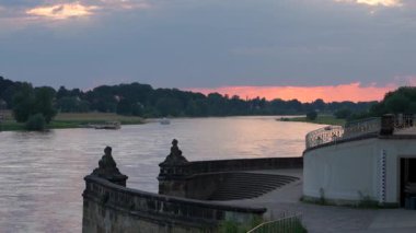 Nehirde güzel bir gün batımı. Demirlemiş bir feribot yolcuları bekliyor. Elbe Nehri yavaşça akar. Küçük kuşlar yiyecek aramak için uçarlar. Dresden, Pillnitz, Almanya