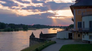 Nehirde turuncu gün batımı. Gün batımında nehir manzarası. İnsanları bir taraftan diğer tarafa naklediyor. Önde küçük bir saray var. Ağır çekim. Elbe Nehri. Dresden, Pillnitz, Almanya 