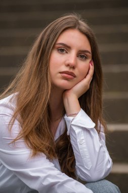 Rüzgarda savrulan uzun saçlı şirin bir kızın yakın plan portresi. Genç bir kadın merdivenlerde oturuyor, eline yaslanıyor ve kameraya bakıyor.
