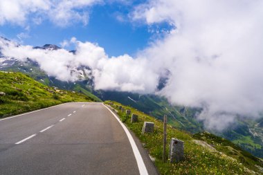  Ünlü dağ yolu, Serpentine Grossglockner-Hochalpenstrasse manzaralı dik dağ yamaçları boyunca rüzgarlar altında. Büyük dağlar bulutlarda gizlidir. Avusturya