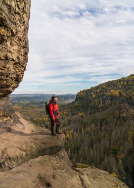 Sırt çantalı ve tripodlu bir fotoğrafçı bir kayanın üzerinde duruyor. Ulusal Park Sakson İsviçre. Almanya