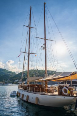 Beyaz bir yat, yelkenleri açık, yazın limana demir atmış. Gemide tatil, yat gezisi. 