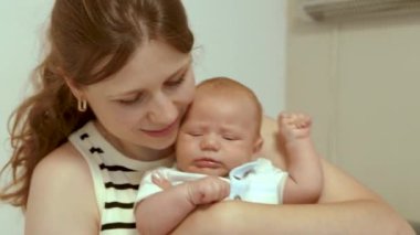Anne ve yeni doğan bebeğin yakın portresi. Anne şefkatle kucağında yeni doğmuş oğlunu tutuyor. Onunla konuşur ve bebeği öper. Mutlu annelik, sevgi ve annelik. yavaş çekim 