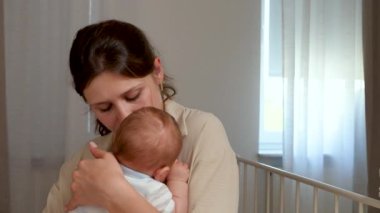 Mutlu bir annenin kucağında yeni doğmuş şirin bir bebeğin görüntüsü. Bakıcı genç anne nazikçe bebeğin başını okşuyor, öpüyor, uyutmaya çalışıyor. Çocukluk kavramı, ebeveynlik. 