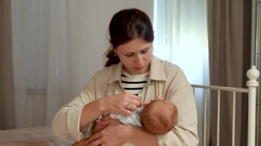   Bakıcı anne, yeni doğmuş bebeğinin kulağını nazikçe siler. Yeni doğmuş bebeğine sevgi dolu bir şekilde bakıyor. Annelik kavramı. Ebeveynlik. Mutlu aile