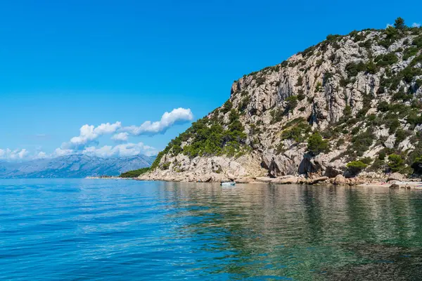 Küçük gemi kayalık kıyı boyunca yelken açar. Denizde saydam su. Hırvatistan. 