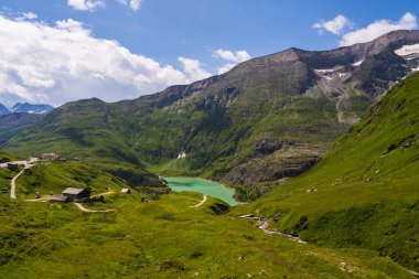 Mountain lake  between green slopes of mountains. Small hous, alpine hotel. Beautiful winding mountain road, Grossglockner High Alpine Road. Austria  clipart