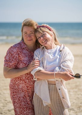 Mutlu, neşeli bir anne ve yetişkin bir kız birbirlerine sımsıkı sarılıyorlar. Mavi deniz arka planı. Güneşli bir gün. Aile ilişkileri. Aile tatili.