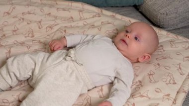  Yeni doğmuş tatlı erkek bebek kanepede yatıyor. Dikkatlice izliyor. Bebek istirahati evde battaniyeyle oynuyor. Mutlu bebek bakımını kabul et