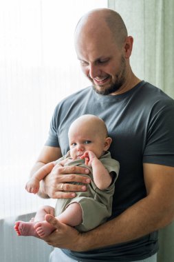 Yeni doğmuş bebeğiyle gülümseyen mutlu babaya yakın çekim. Baba şefkatli aile anlarından, babalıktan, bebeğe bakmaktan hoşlanıyor..