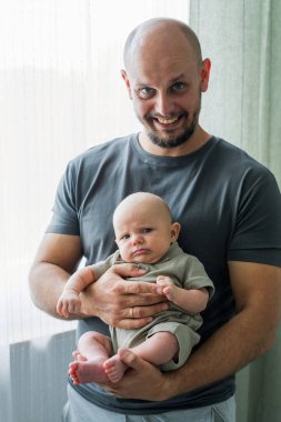 Yeni doğmuş bebeğiyle gülümseyen mutlu babaya yakın çekim. Baba şefkatli aile anlarından, babalıktan, bebeğe bakmaktan hoşlanıyor..