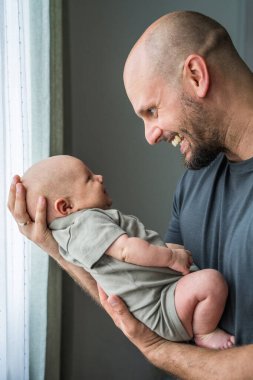 Yeni doğmuş bebeğiyle gülümseyen mutlu babaya yakın çekim. Baba şefkatli aile anlarından, babalıktan, bebeğe bakmaktan hoşlanıyor..