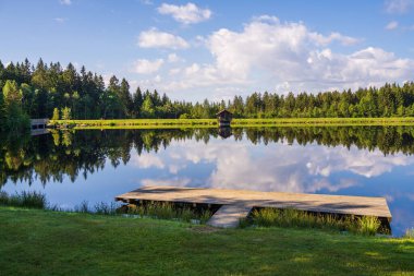 Almanya 'daki ladin ormanları arasında bulutların yansımasıyla güzel, küçük mavi bir dağ gölü. Ön planda ahşap bir köprü var. Fichtelsee 'de. Bavyera 'da. Almanya