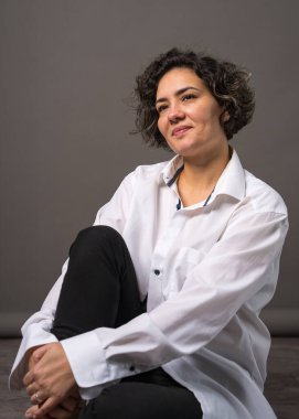 Mükemmel beyaz dişleri olan güzel bir kadın yerde oturur ve kameraya bakar. Gri bir arkaplan ile izole edilmiş.