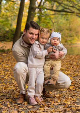 Mutlu, gülümseyen baba küçük oğlunu ve kızını kollarında tutuyor. Açık havada mutlu bir aile fotoğrafı. Babalık. Sevgi. Çocukluk