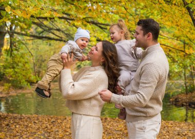 İki çocuklu mutlu bir aile. Anne ve baba kucağında küçük bir kız ve oğlan. Sonbahar parkında çocuklarla yürümek.