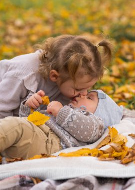 Cute brother and sister in the fall park. Girl 3 years old gently kissing her brother's boy. Love. Family. Happy childhood clipart