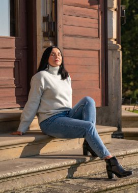 Rahat kadın merdivenlerde oturuyor, rahat, yün kazak giyiyor. Gündüz gözüyle bak. konsept: konfor, şehir tatili, hafta sonu.