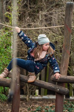 Sevimli küçük kız yılın daha serin mevsiminde çocuk parkında eğleniyor.
