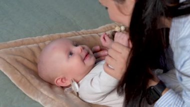 Bebek yatakta yatıyor. Anne yeni doğmuş bir bebekle konuşuyor. Bebek dikkatle izliyor ve tekrar etmeye çalışıyor. Kapatın. Öğretmenlik. Çocuk gelişimi. 4k görüntü