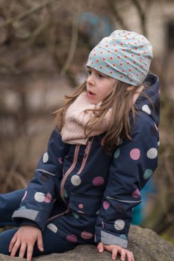 Açık havada bir kayanın üzerinde oturan sevimli küçük bir kızın portresi. Çocuk dalgın dalgın uzaklara bakıyor..