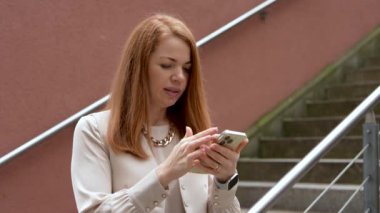 Şık giyinmiş şirin bir kız telefonu elinde tutuyor ve bilgileri yoğun bir şekilde arıyor. Sahne sokakta geçiyor, atmosfer yaratıyor modern şehir ritim hayatı. Yavaş çekim
