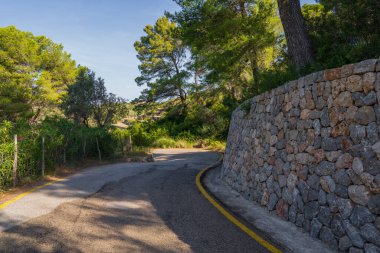 İspanya 'nın Mallorca kentinin manzaralı Akdeniz manzarasıyla çevrili geleneksel taş duvarın yanında uzanan sessiz asfalt yol.