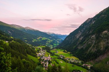 Avusturya 'nın Heiligenblut kentinin gün batımındaki en görkemli manzarası. Sıcak altın ışık, engebeli dağ zirveleri ve tuhaf alp mimarisini yıkıyor.