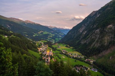 Avusturya 'nın Heiligenblut kentinin gün batımındaki en görkemli manzarası. Sıcak altın ışık, engebeli dağ zirveleri ve tuhaf alp mimarisini yıkıyor.
