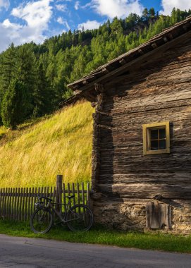 Avusturya 'nın Heiligenblut kasabasında kırsal ahşap evin yanına park edilmiş modern bisiklet. Büyüleyici bir macera ve gelenek, manzaralı alp arka planına karşı kurulmuş.