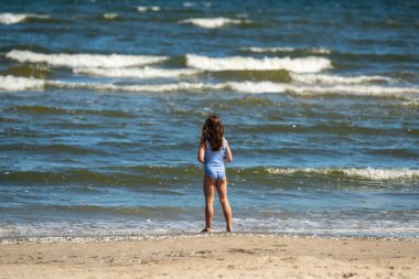 Kameraya arkası dönük şirin küçük kız Baltık Denizi 'ne bakıyor. Huzurlu deniz huzurlu bir atmosfer yaratır. Anlık yansıma, merak, sükunet, doğanın güzelliği..