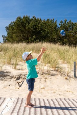 Genç çocuk Baltık Denizi sahilinin kumullarında top oynuyor, güneşli ve kaygısız atmosferin tadını çıkarıyor. Kavram: çocukluk, açık hava aktiviteleri, aile tatilleri, sahil tatilleri ve kaygısız anlar