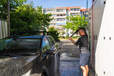 Adam arabasını su ve sabunla yıkıyor, araba bakımına odaklanıyor, arabayı temiz tutuyor ve görünüşüne özen gösteriyor. self-servis kavramı